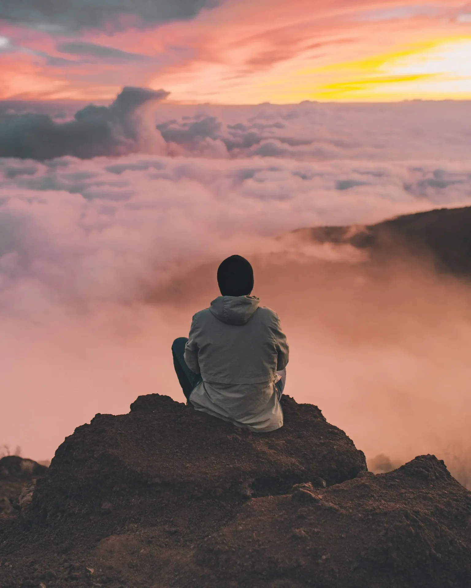 ian-stauffer-uftqFbfWGFY-unsplash Person sitting on a mountain overlooking clouds at sunrise.